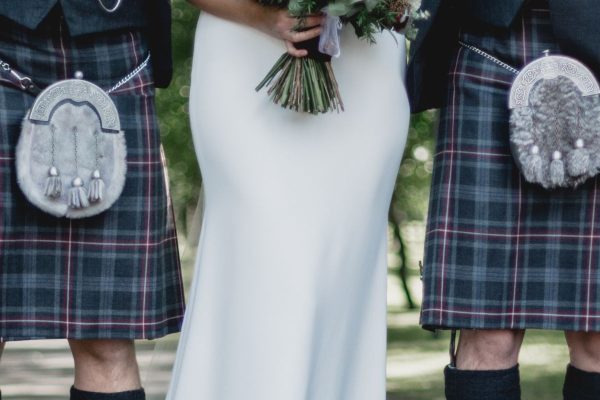 Scotsmen dressing in kilt on wedding day with bride in the middle.